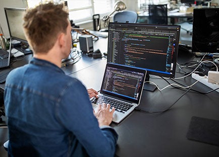 Student looking at multiple computer screens with code on them
